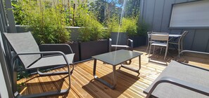 Un patio exterior con sillas y mesa de metal, rodeado de macetas y una terraza de madera.
