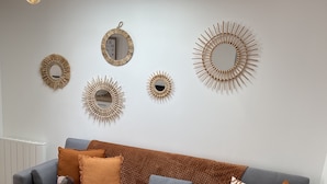 A living room with a grey sofa, brown and patterned cushions, a small table with candles, and wall-mounted decorative mirrors. - LE POULORIO TERRASSE - T3 RDC - 2 salles de douches  * ByLocly * (Lorient)