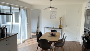 A modern kitchen with a dining area, featuring a wooden table, black chairs, and a pendant light. - LE POULORIO TERRASSE - T3 RDC - 2 salles de douches  * ByLocly * (Lorient)