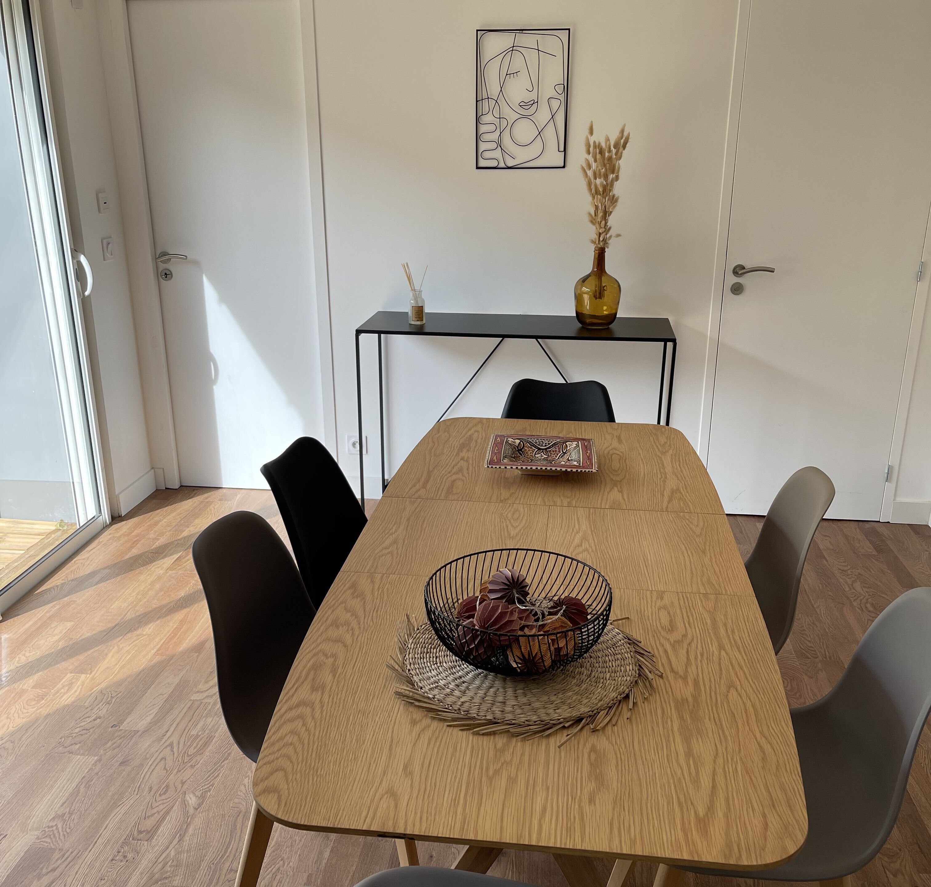 A conference room with a wooden table, black chairs, a small black table with a vase and candle, and a framed artwork on the wall.
