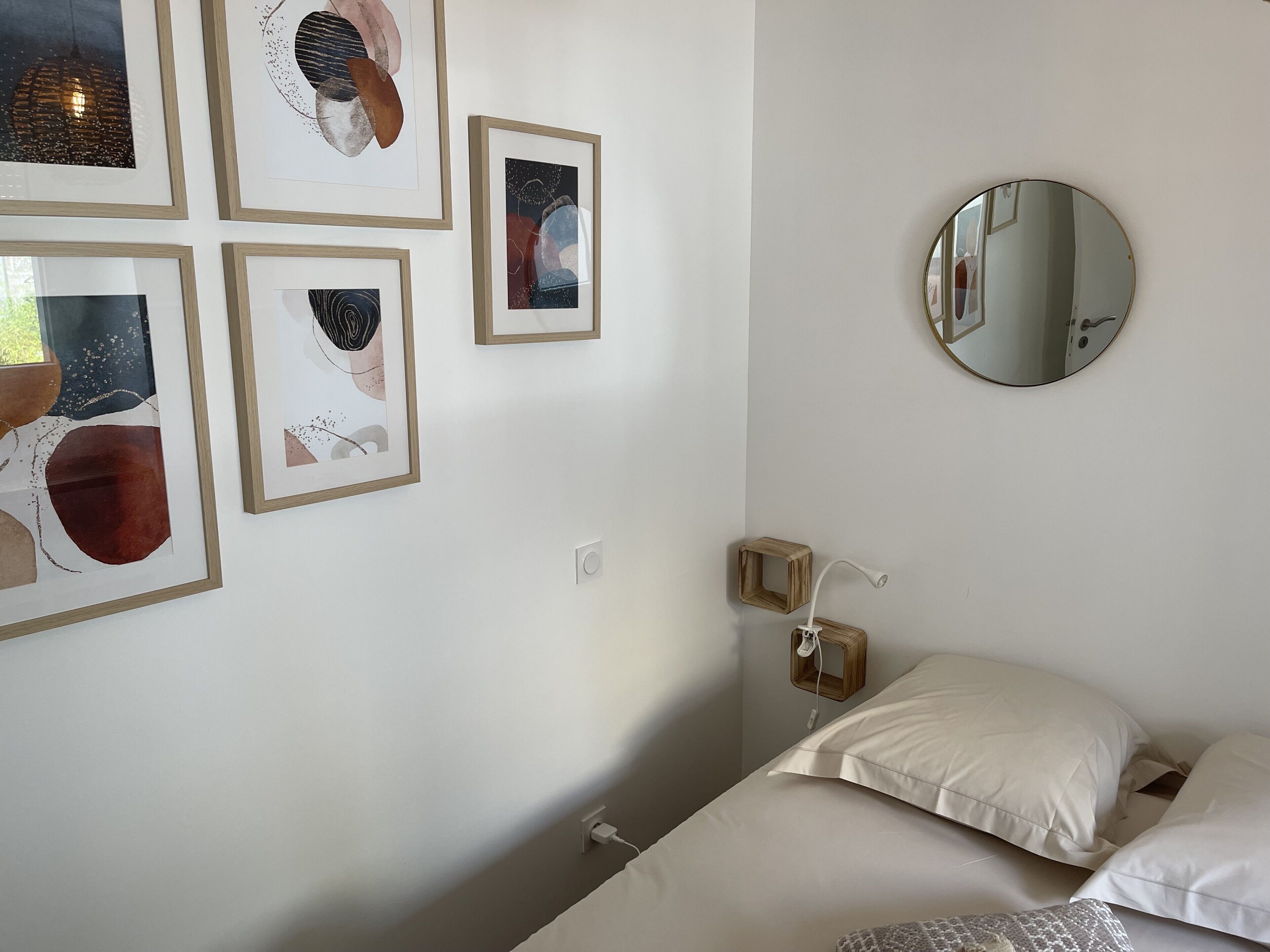 A bedroom with a bed, pillows, a bedside table, a mirror, and framed artwork on the wall.
