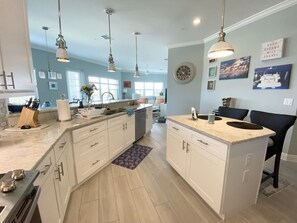 A modern kitchen with white cabinetry, a large island, pendant lighting, and a clock on the wall.
