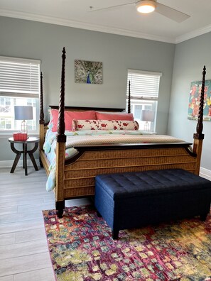 A bedroom with a four-poster bed, a small round table with a lamp, and a colorful rug.
