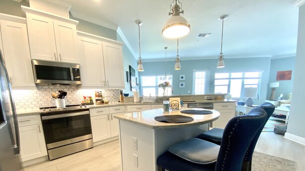 A modern kitchen with white cabinets, stainless steel appliances, and a central island with bar stools. - 5 Star Resort Style Luxury Condo top floor bay views 3 miles to Beach (Bradenton)