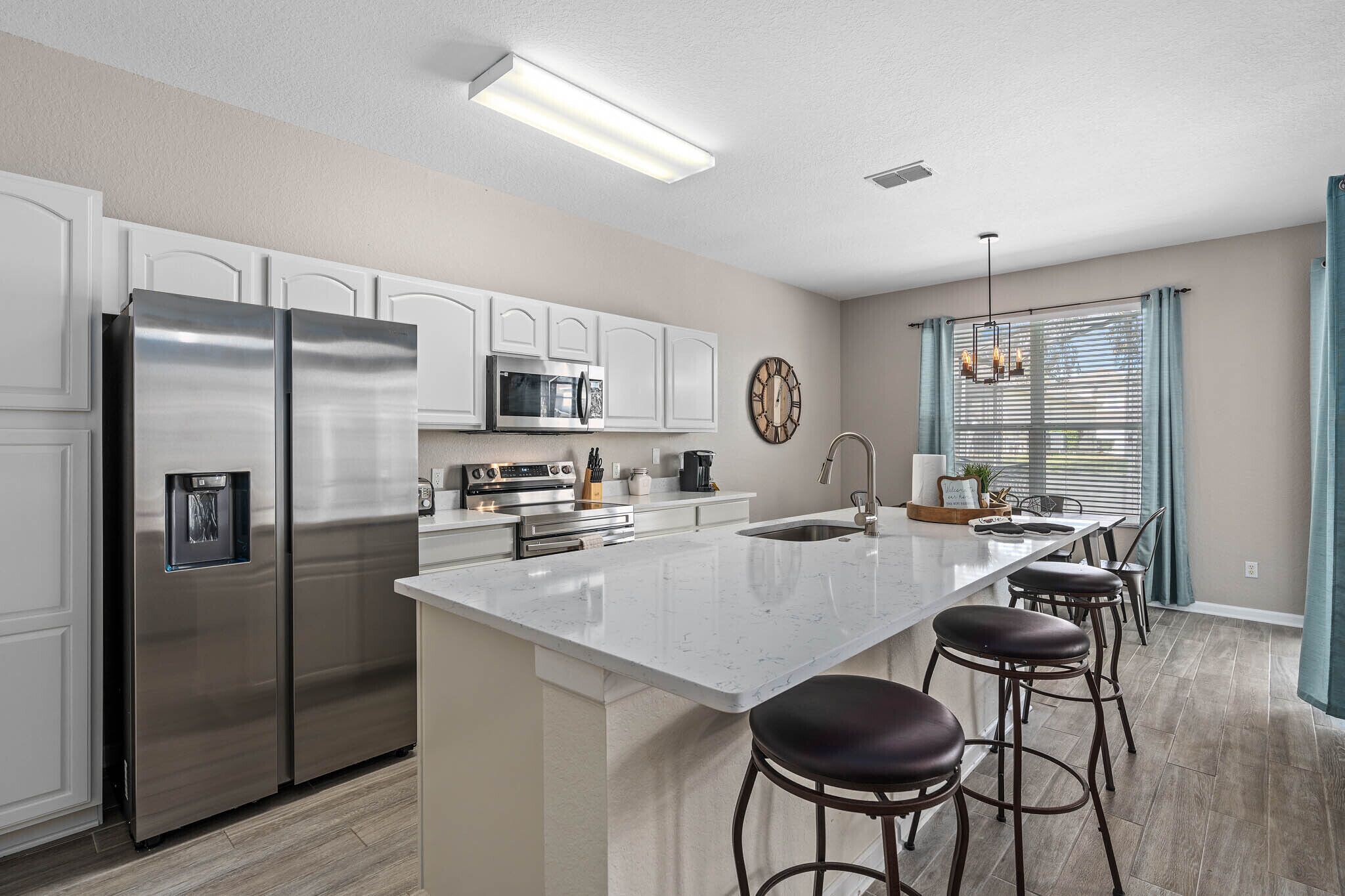 A modern kitchen with stainless steel appliances, a large island with bar stools, and a window with curtains.
