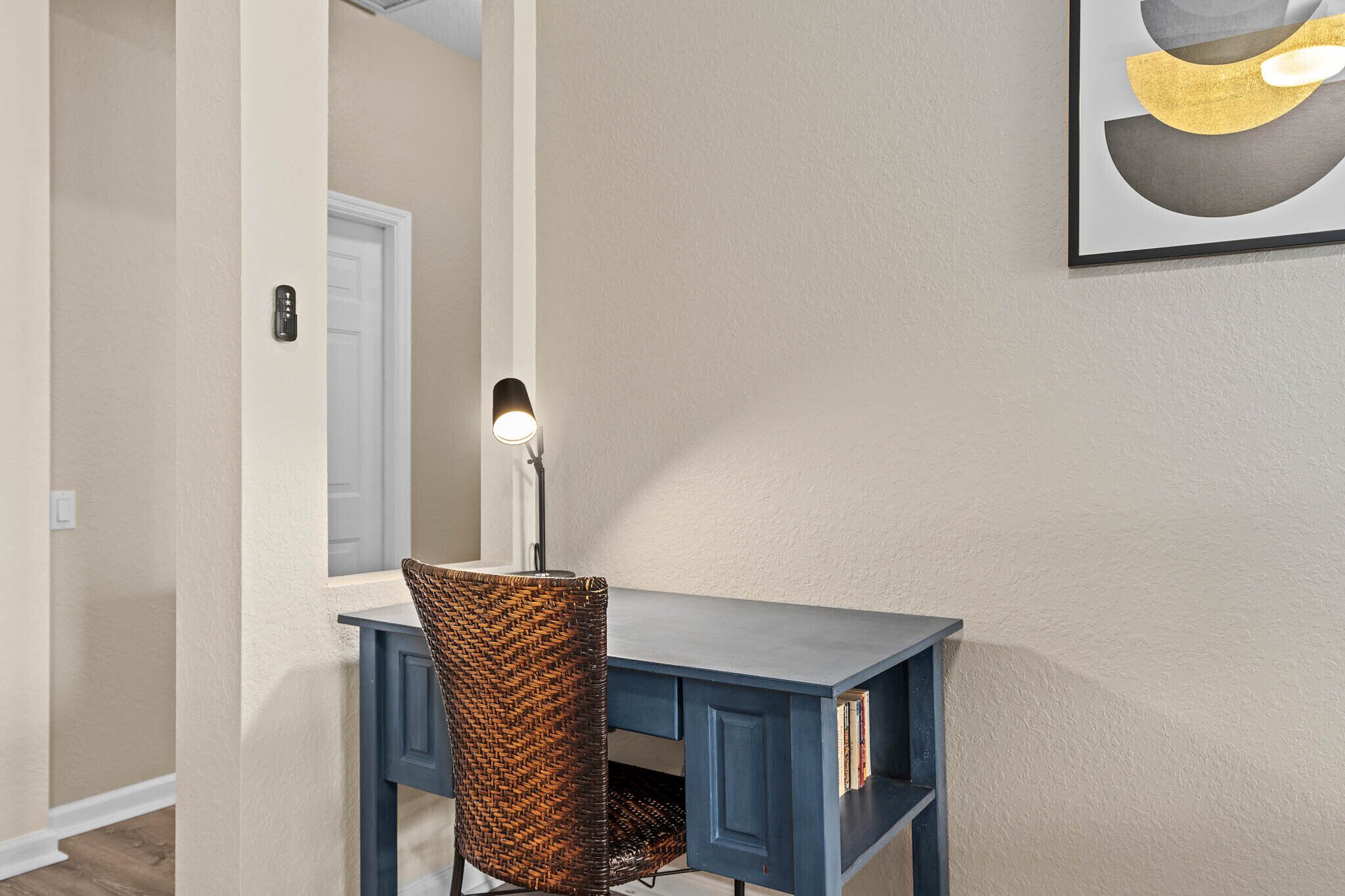 A room with a desk, chair, and a framed picture on the wall.