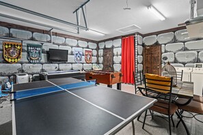 A room with a ping pong table, foosball table, and a television. There are several coats of arms on the wall.