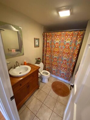 Une salle de bain avec un meuble-lavabo en bois, un lavabo blanc, des toilettes et un rideau de douche à motifs.