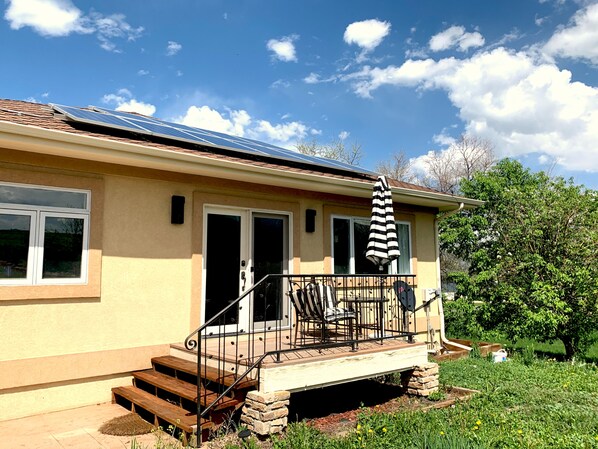 Une maison avec un toit équipé de panneaux solaires, un porche à l’avant avec un banc et un petit jardin.