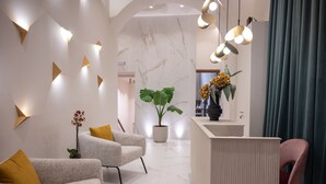 Un área de recepción moderna con una pared de mármol, un mostrador de recepción y dos sofás con cojines amarillos.