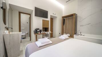 A modern hotel room with a large bed, a bathroom with a bathtub, a desk with a chair, and a flat-screen TV mounted on the wall.