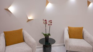 Dos sillones con cojines color mostaza, una mesita redonda con una orquídea en maceta e iluminación de pared geométrica.