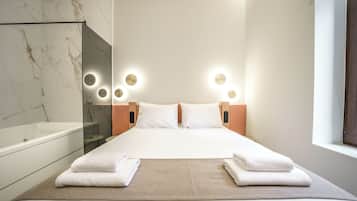 A hotel room with a large bed, a glass-enclosed shower, and a view of the sky through a window.