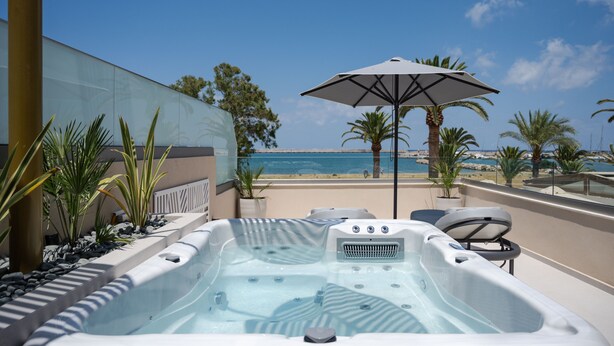 Un jacuzzi con vistas a la playa y al océano, rodeado de palmeras y plantas en macetas.