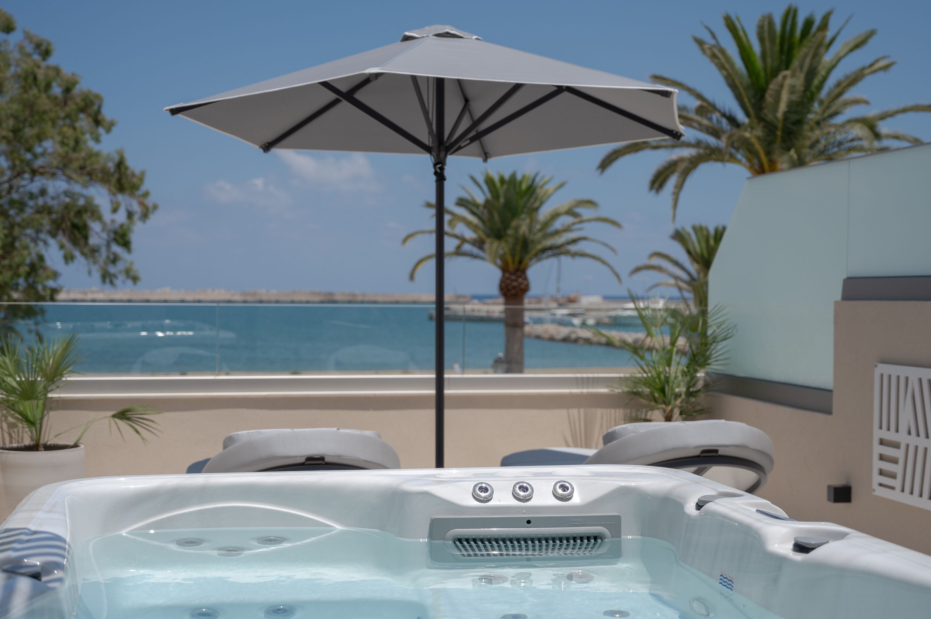 A hot tub with an umbrella, a poolside view, and palm trees.