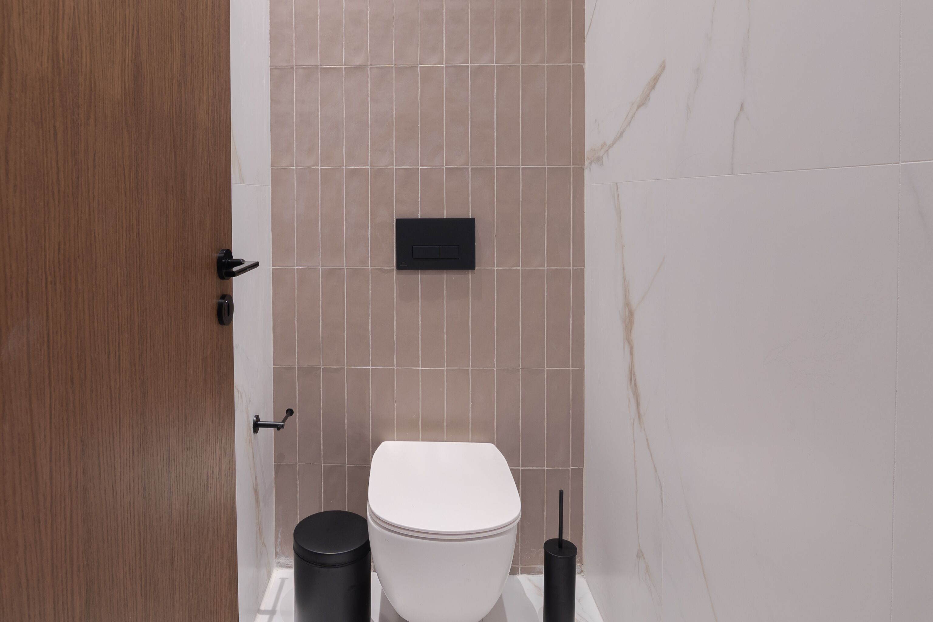 A modern bathroom with a white toilet, a black trash bin, and a black toilet brush.