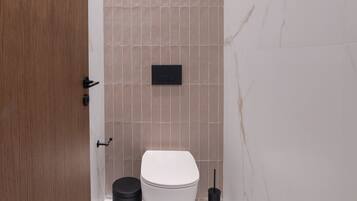 A modern bathroom with a white toilet, a black trash bin, and a black toilet brush.