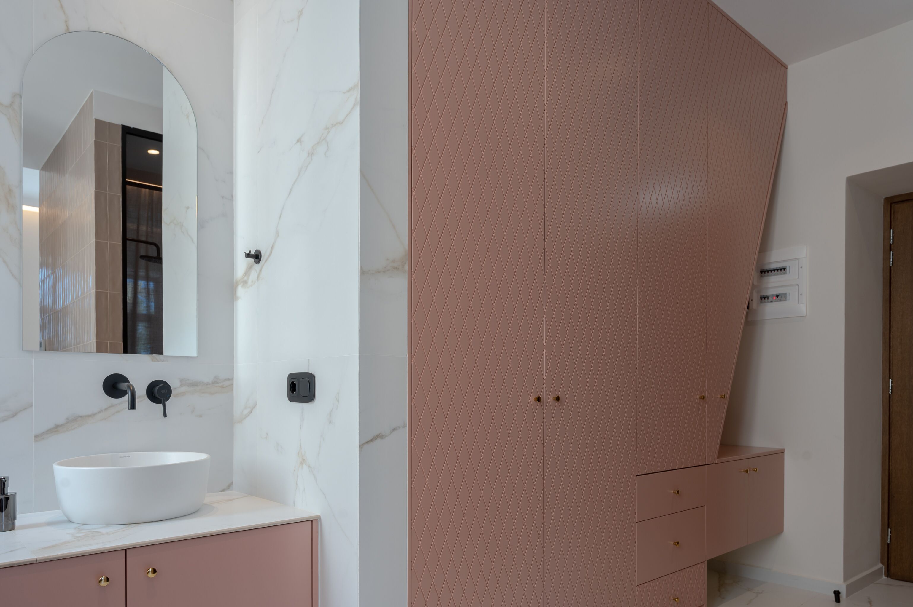 Un baño con lavamanos de mármol blanco, un espejo grande y un mueble rosa con cajones.