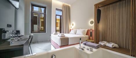 A modern hotel room with a large bathtub, a bed with white linens, a desk with a chair, and a large mirror.