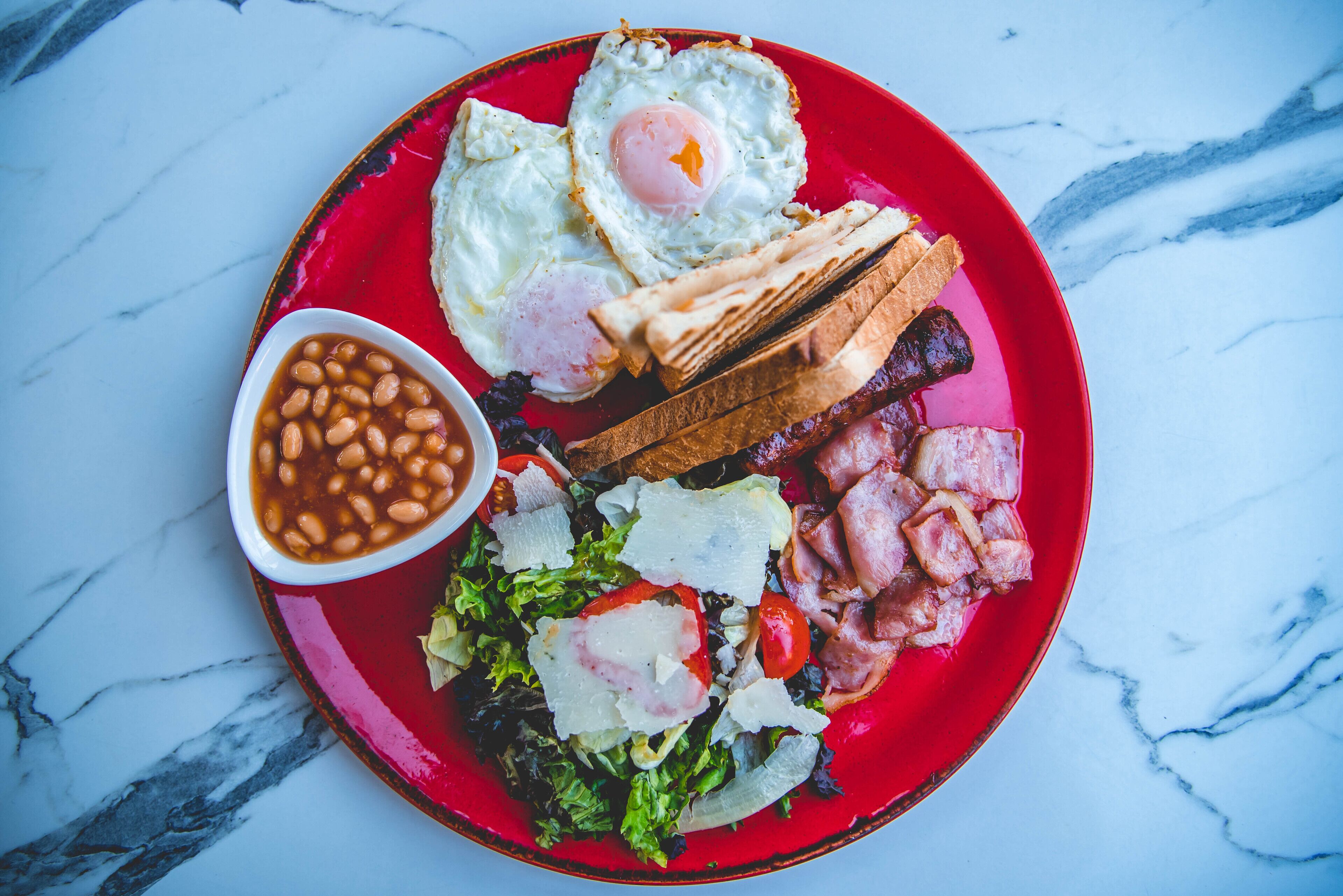 Un plato de comida con huevos, frijoles, tocino y tostadas sobre un plato rojo.