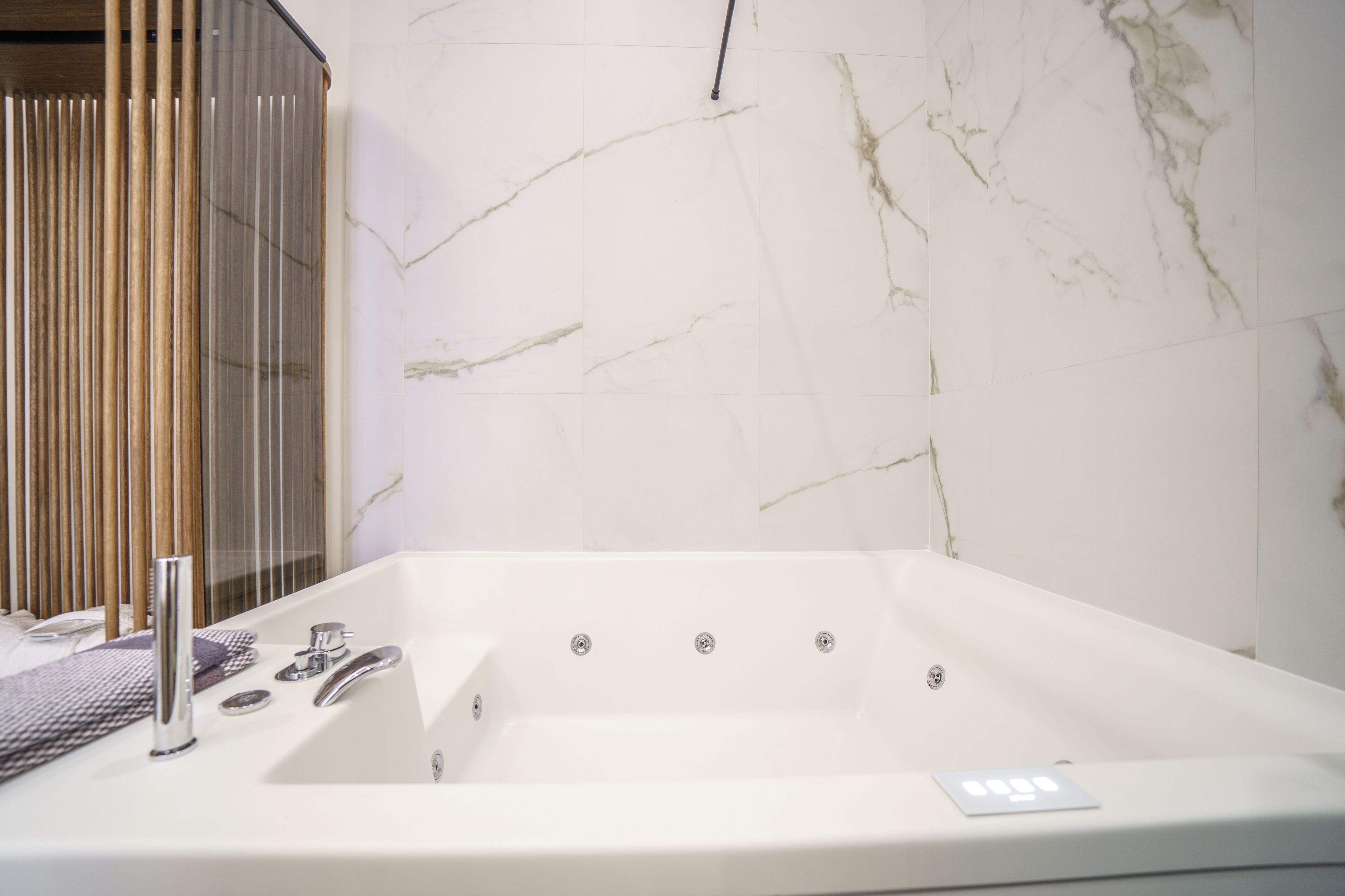 Une salle de bain moderne avec un mur en marbre, une baignoire et un espace douche.