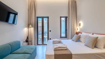 Una habitación de hotel con cama, un sofá azul, un televisor montado en la pared y un balcón con cortinas.