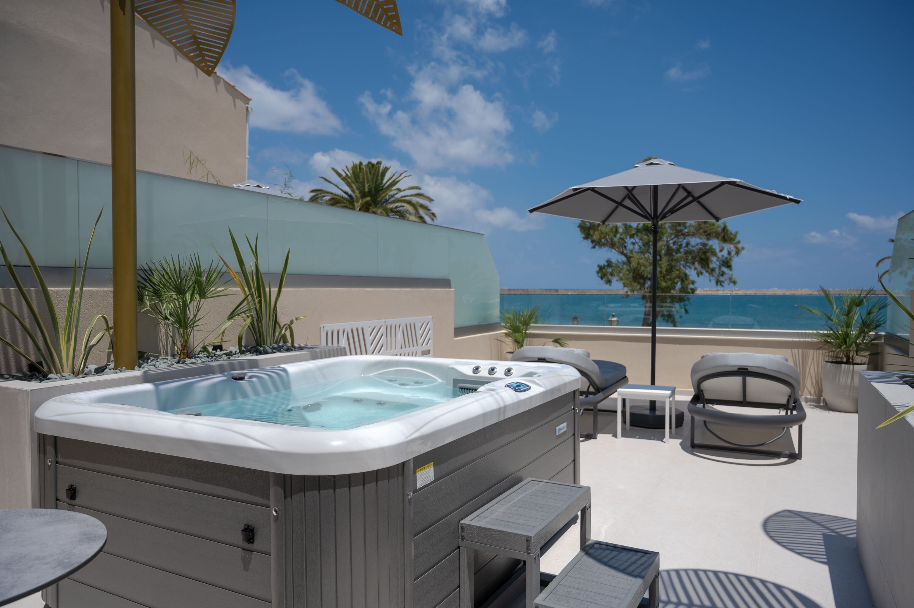 A rooftop pool area with a hot tub, lounge chairs, and an umbrella.
