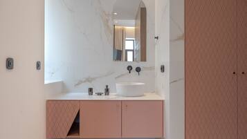 A modern bathroom with a white marble wall, a large mirror, a round sink, and pink cabinets.