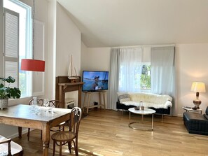 Uma sala de estar ampla com uma mesa de jantar de madeira, cadeiras, uma televisão, um sofá e um abajur.