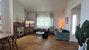 Un salon avec un plancher en bois, un canapé, un téléviseur, une table à manger avec des chaises et une fenêtre avec des rideaux.