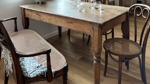 Un coin repas avec une table en bois, des chaises en osier et une lampe suspendue rouge.