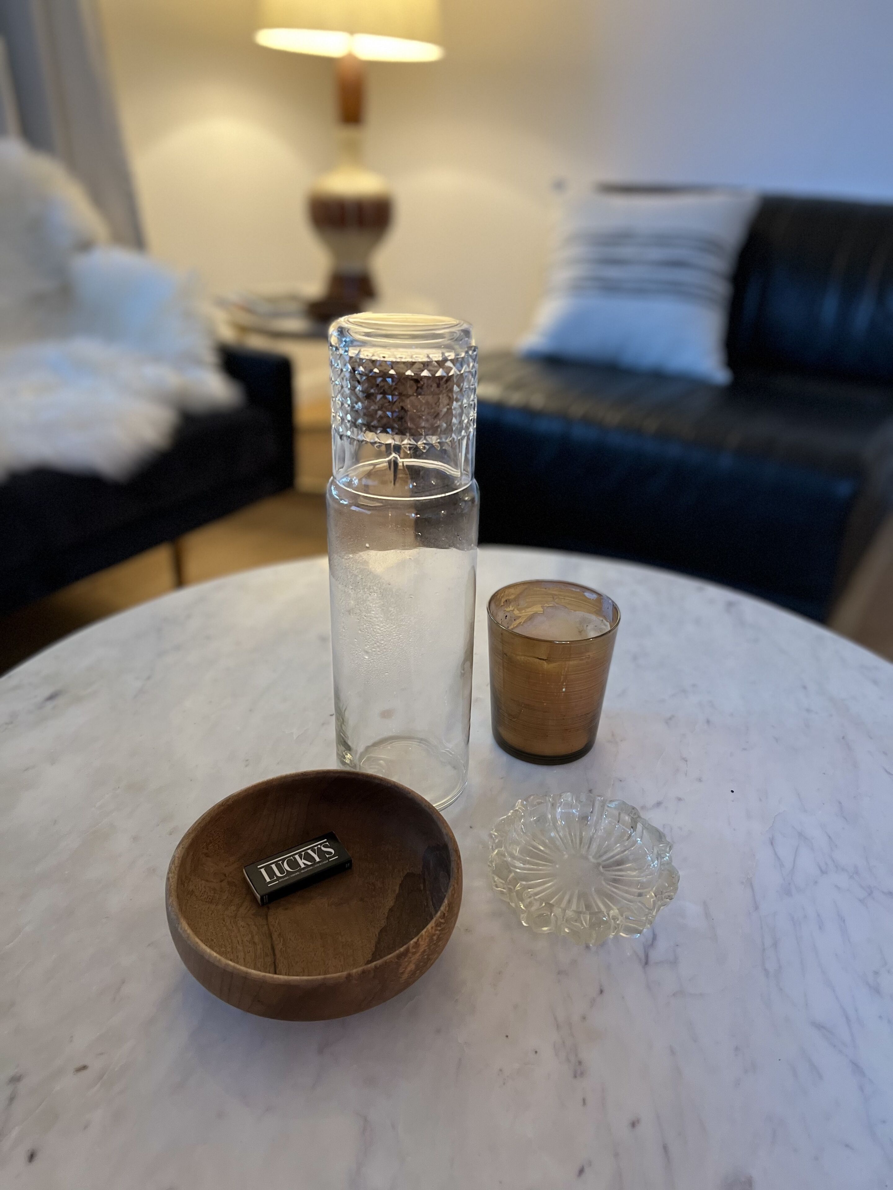 A clear glass bottle, a wooden bowl with a label, and a glass cup on a marble table.