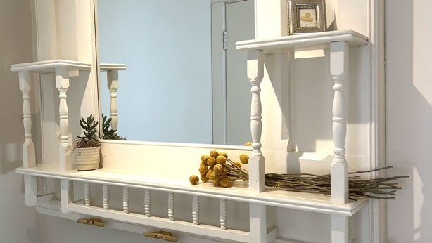 Une étagère blanche fixée au mur, agrémentée d’un miroir, de deux petites plantes en pot et d’un objet décoratif.