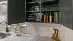 Een keuken met een wit bekleurd aanrechtblad, een zwart kastje met open vakken met heldere containers en keukengerei in goudkleur.