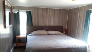 Makuuhuone, jossa on suuri sänky, puupaneloidut seinät, yöpöytä ja peili.