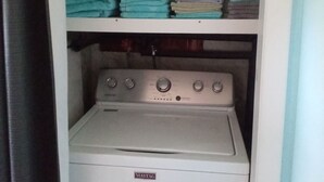 Pesuhuone, jossa on Maytag-merkkinen pesukone ja -kuivausrumpu, hyllyjä, joilla on siististi taiteltuja pyyhkeitä, sekä pullo valkaisuainetta.