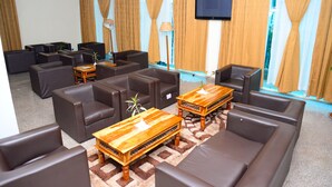 A modern hotel lobby with leather sofas, wooden coffee tables, and a flat-screen TV mounted on the wall. - Golden Royale Hotel (Enugu)