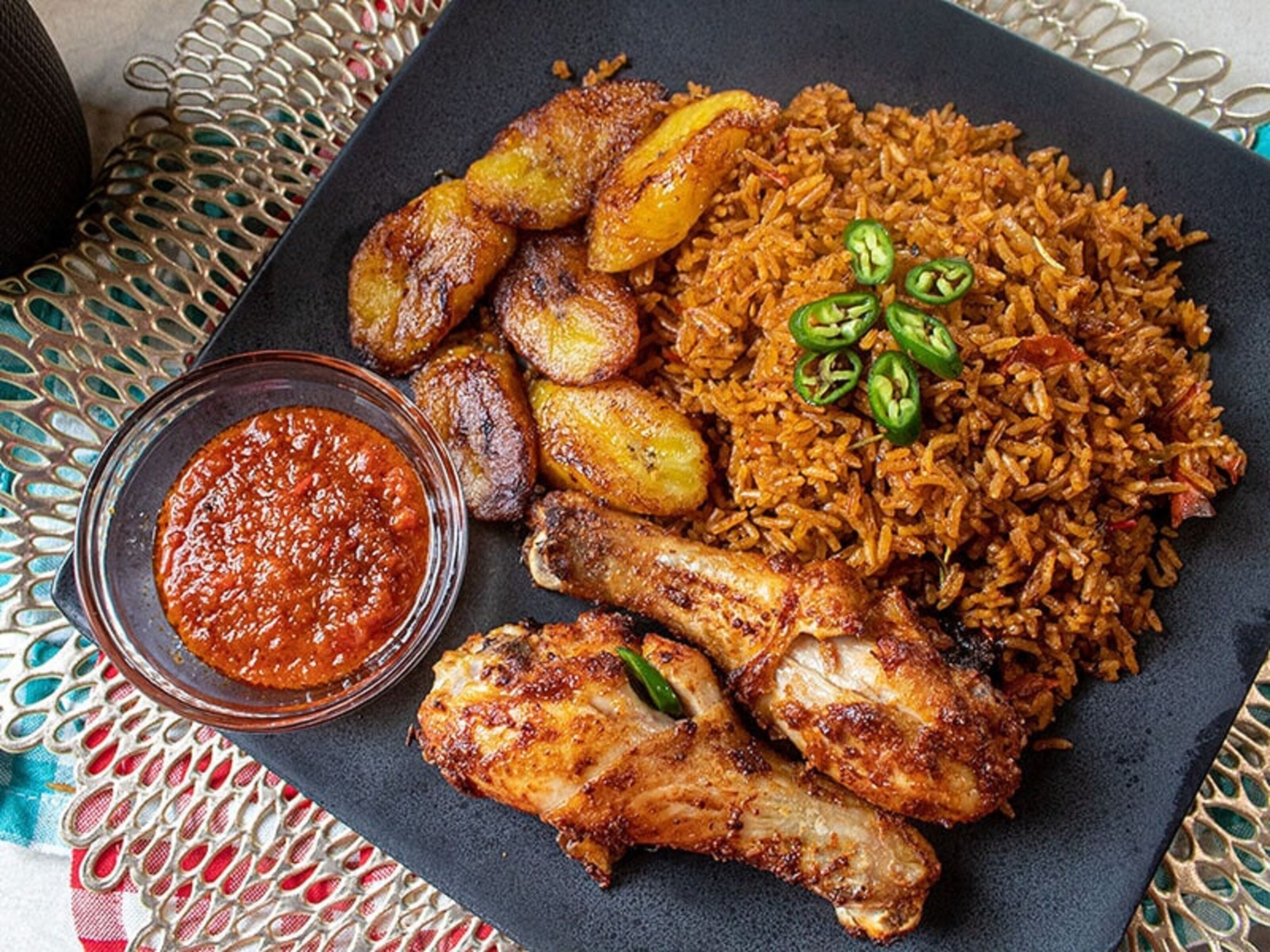 A plate of food with rice, chicken, plantains, and a side of sauce.