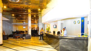 A hotel lobby with a reception desk, seating area, and a large mirror. - Golden Royale Hotel (Enugu)