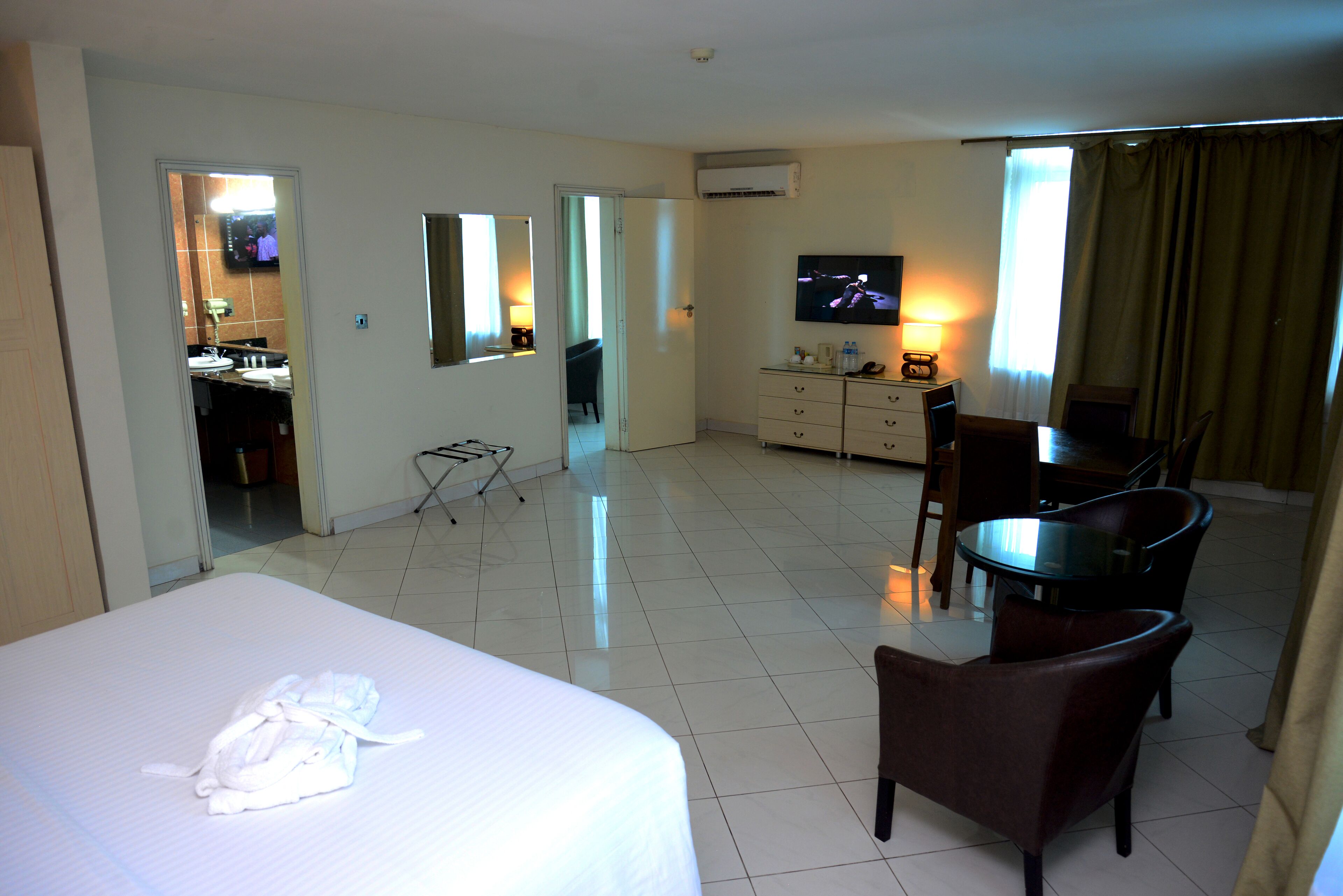A hotel room with a bed, a desk, a chair, a television, and a bathroom visible through an open door.