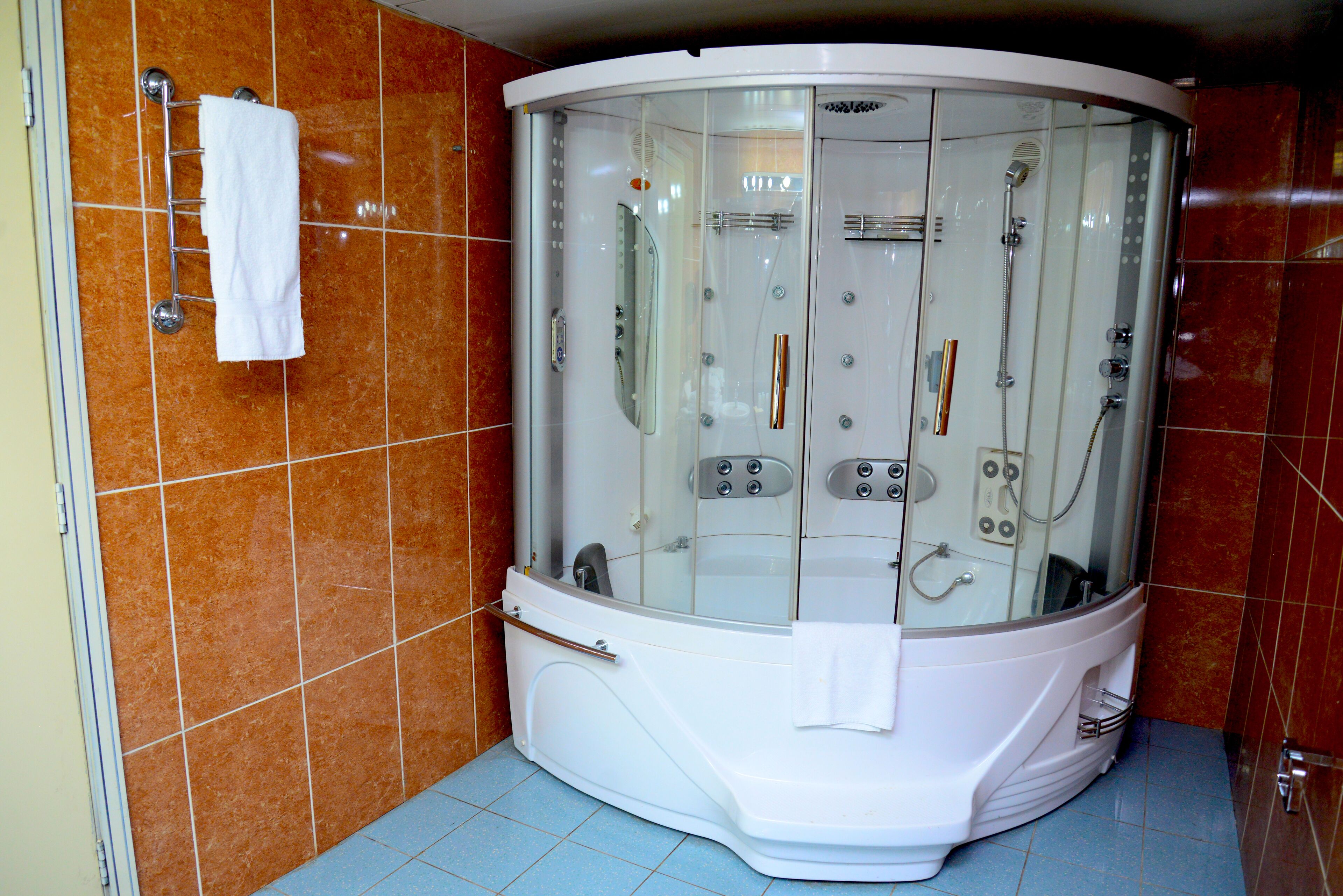 A modern bathroom with a glass-enclosed jacuzzi, a white towel rack, and a tiled floor.