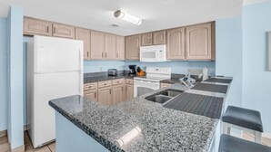 A modern kitchen with granite countertops, a refrigerator, microwave, stove, and sink. - Stunning Views in Atlantica Resort (Myrtle Beach)