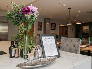 A dining area with a table set for two, a vase with flowers, and a framed menu on the table.