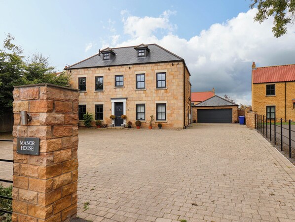 A stone building with a sign reading 'MANOR HOUSE,' a paved driveway, and a garage.