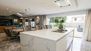 Una cocina moderna con una isla de mármol, comedor con sillas y vista al jardín trasero.