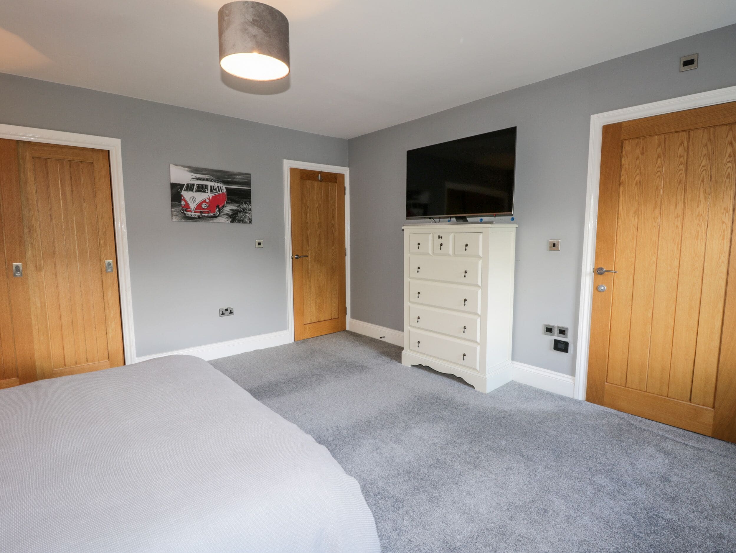 A bedroom with a bed, a dresser, a television, and two doors.
