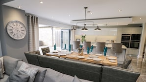 Una sala de estar moderna con un sofá gris y una zona de comedor con una mesa de madera dispuesta para cuatro comensales.