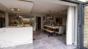 Una cocina moderna con encimera de mármol, un comedor con mesa y sillas de madera, y una pared de piedra.