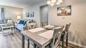 Ein modernes Wohnzimmer mit Essbereich, grauen Wänden, Holzmöbeln und einer Deckenleuchte.