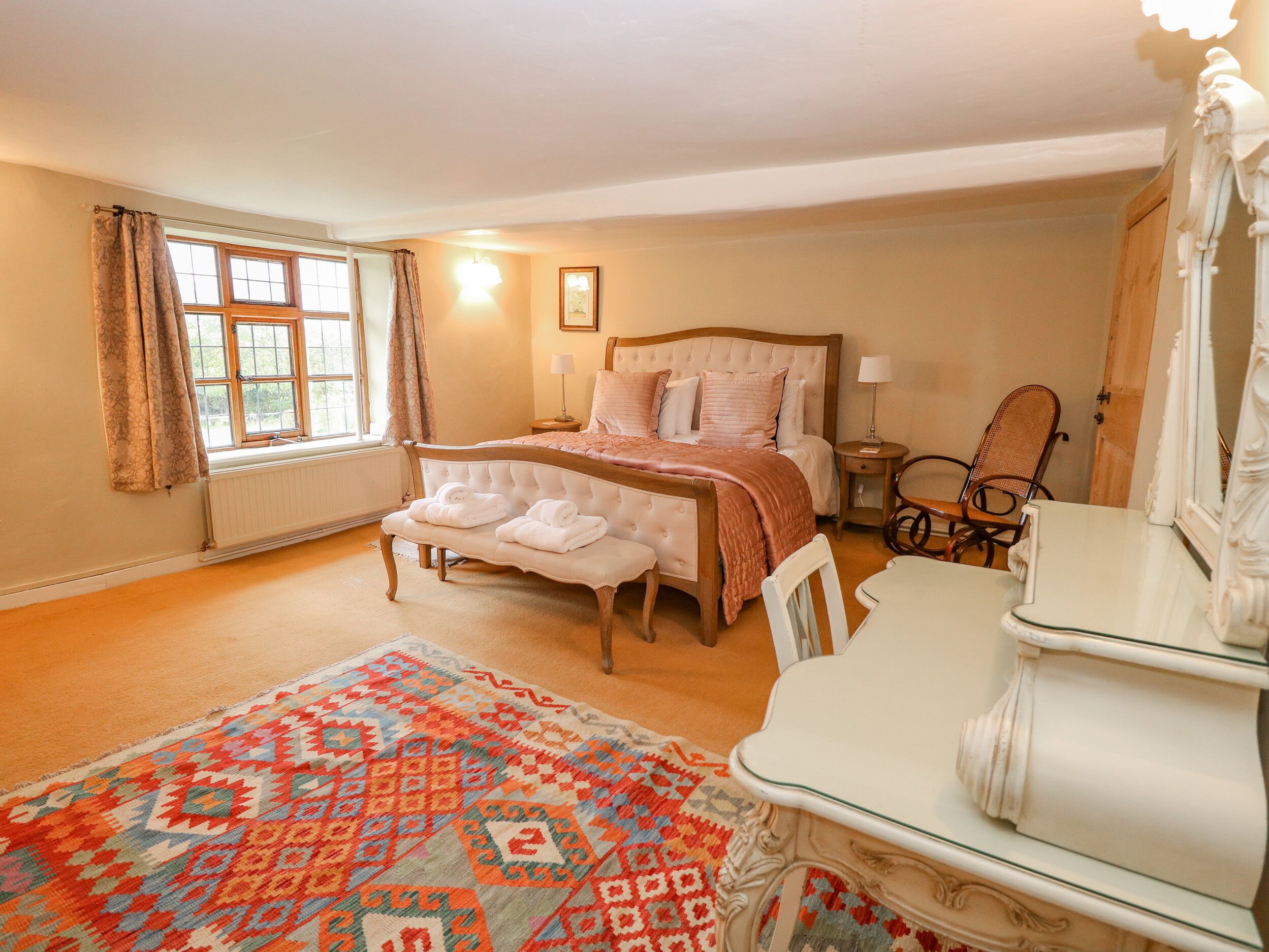 A bedroom with a bed, bedside tables, a chair, a table, and a patterned rug.